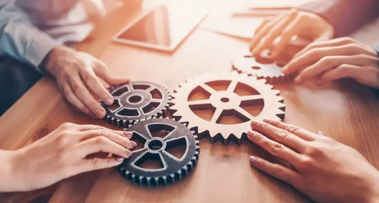 image 2 - White Space | Digital Marketing Agency Group of people assembling interlocking gears on a wooden table, symbolizing teamwork and collaboration.